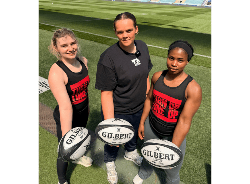 three women holding a rugby ball looking up